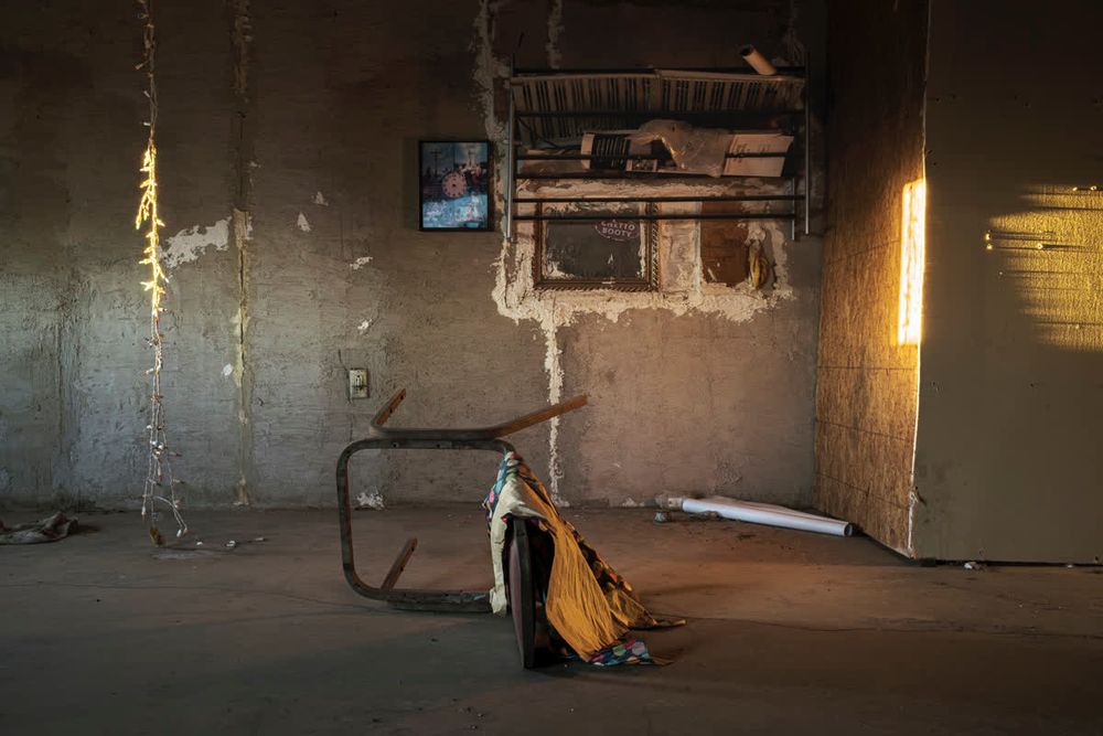 Overturned chair in abandoned cabin, with string of Christmas lights and interior wall lit by sunrise.