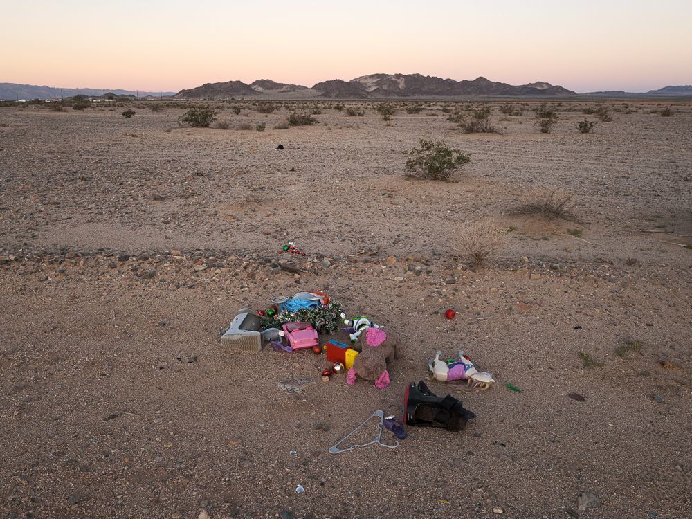 A pile of brightly colored discarded toys in desert landscape with moutain in background.