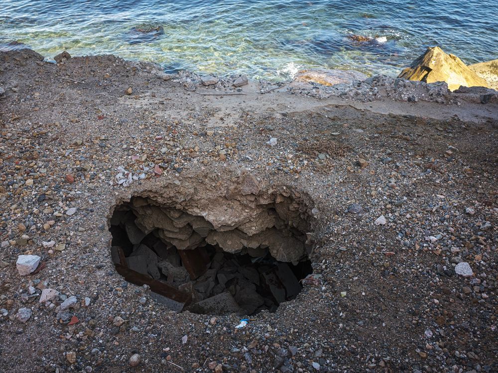 Sinkhole in shady foreground with sunlit sea and rocks in background, seemingly on the same plane.