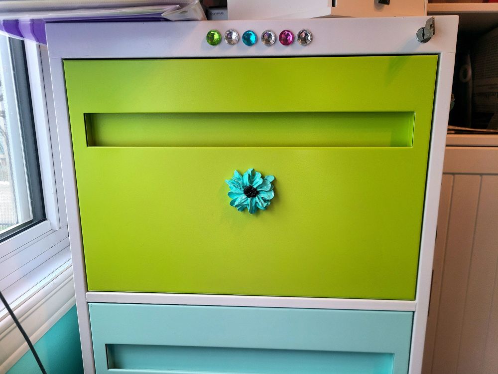 A textured paint flower, hand painted, on the green drawer of a filing cabinet. 