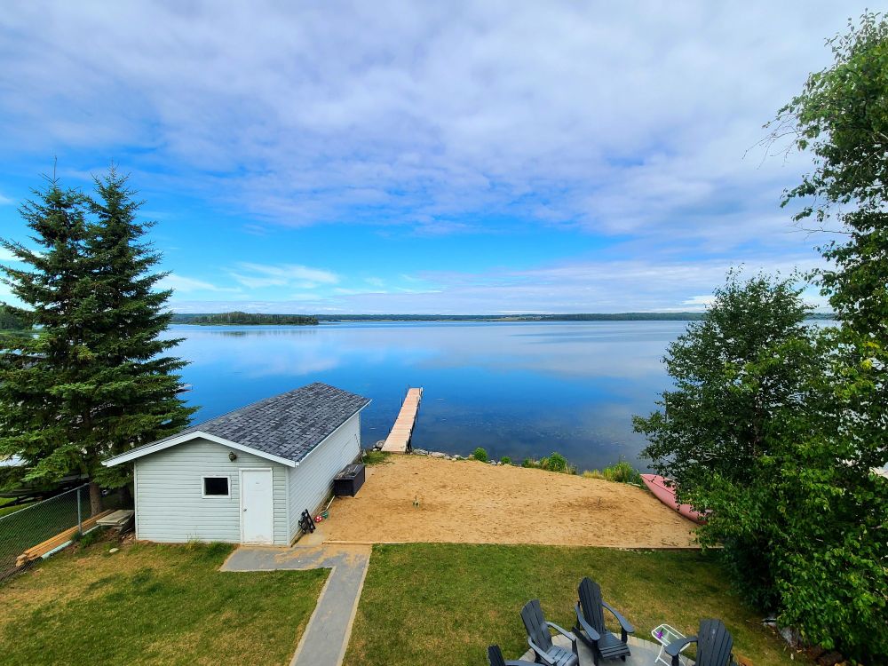 View of a lake, dock, boathouse, and trees from a high up deck. 