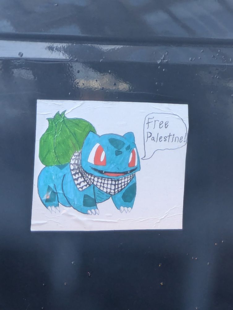 A hand-drawn bumper sticker of the Pokémon Bulbasaur wearing a keffiyeh with a speech bubble that says "free Palestine"