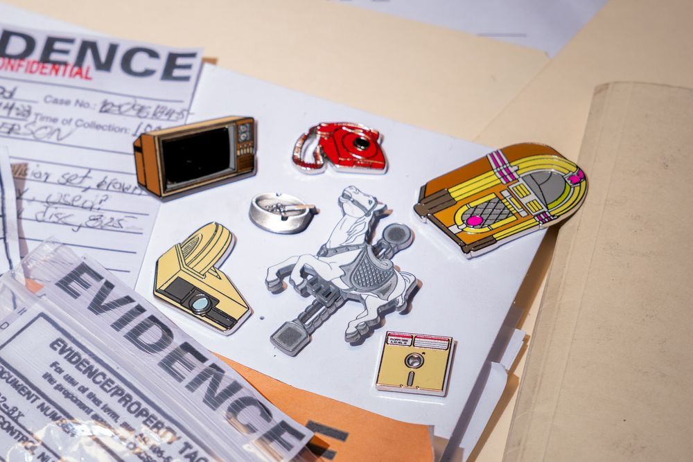 A selection of metal pins featuring various Objects of Power from Control. Including the jukebox, slide projector, carousel horse, floppy disk, telephone, TV, and ashtray.