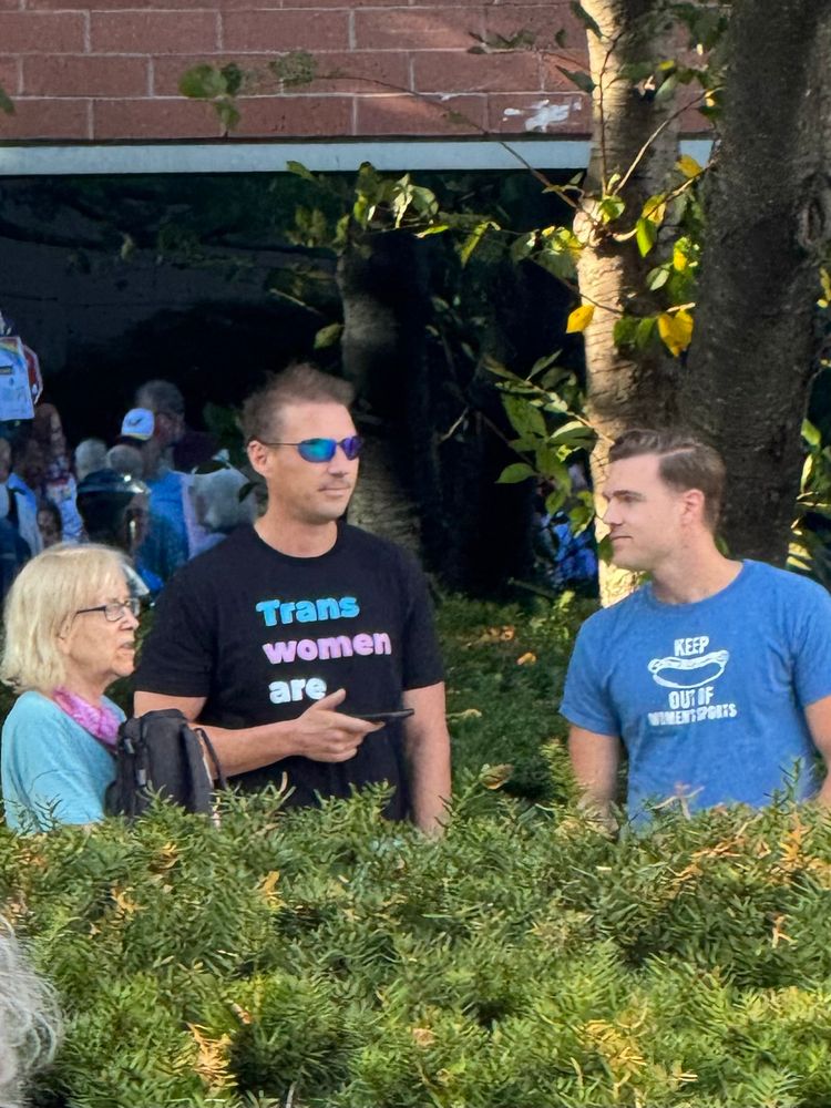 Douchebags with obnoxious shirts. Left is “trans women are men” and the right has “keep” a picture of a hot dog “out of women’s sports.”