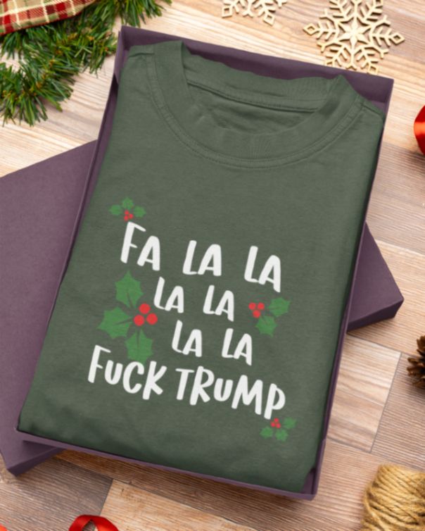 Green T-shirt in gift box with text: "Fa la la la la la la la Fuck Trump" surrounded by holly leaves and berries.