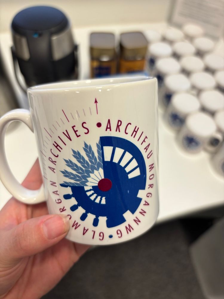 A white woman’s hand holding a mug with a blue logo up.   