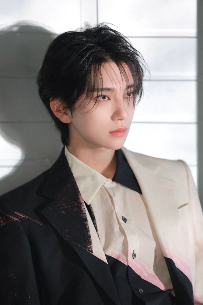 Joshua Hong wearing a black and cream suit and staring off camera seductively.