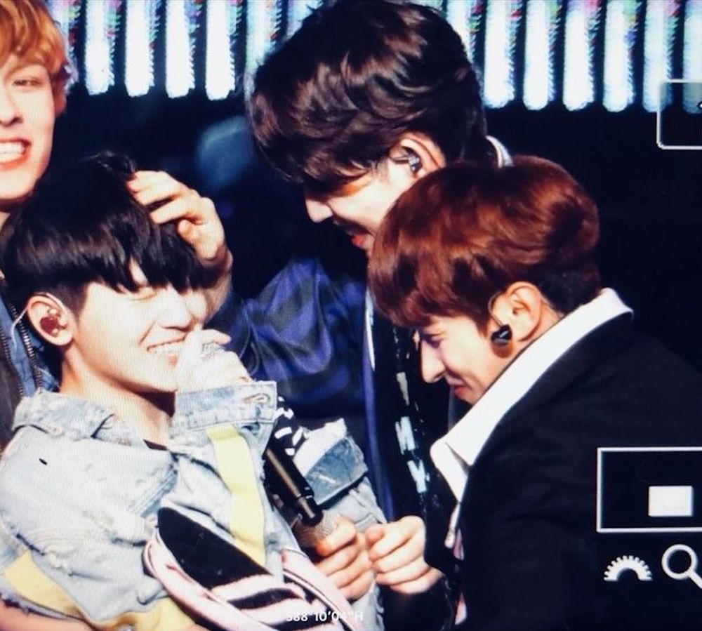 Choi Seungcheol and Lee Seokmin looking very fondly at Lee Jihoon who is smiling with his eyes closed and holding a microphone.