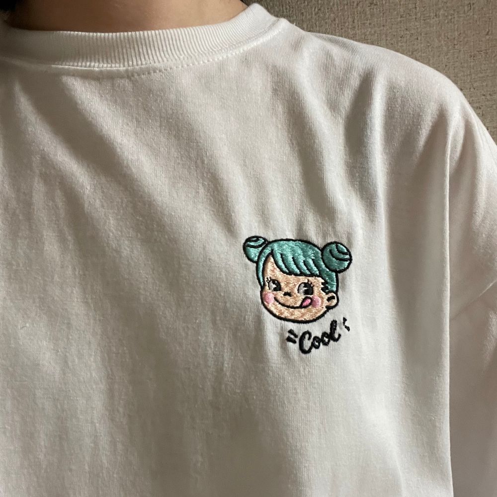 水色の髪色でツインテールをお団子にしたヘアスタイルのペコちゃんが胸元についたTシャツを、ペコちゃんをアップにして撮影した写真