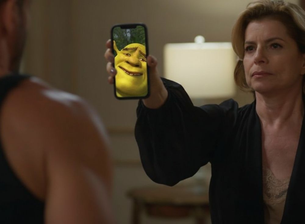 Montagem de uma cena onde Odete está segurando um celular onde se vê na tela o rosto do Shrek fazendo uma careta.