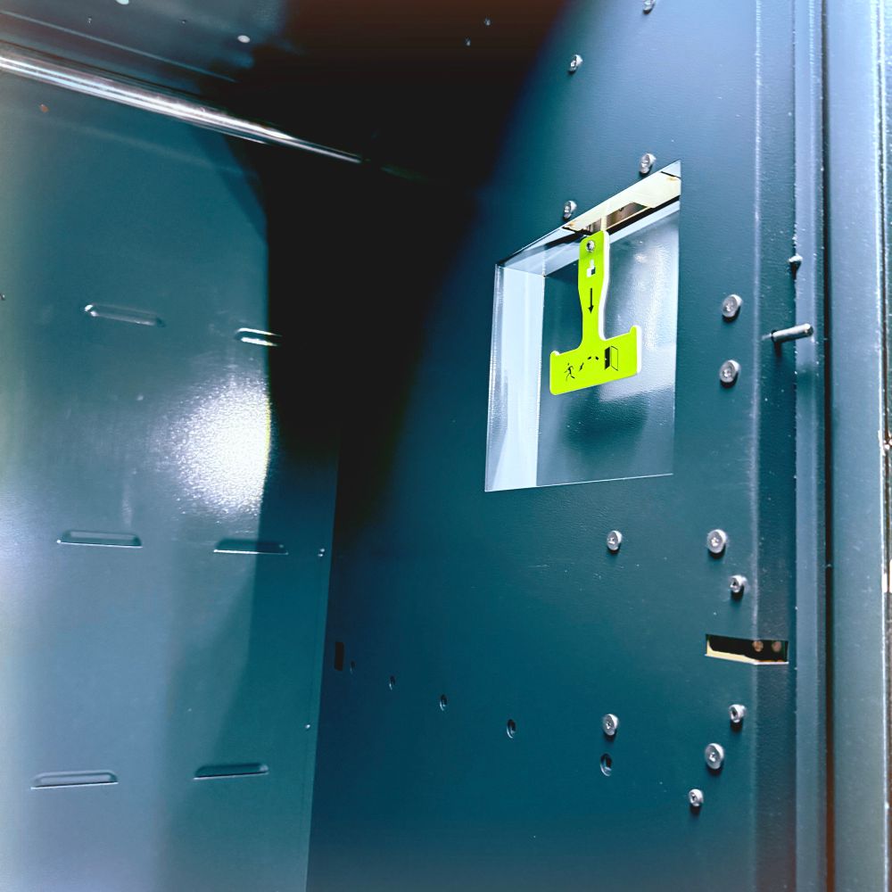 the inside of a gray amazon package locker. the left side of the locker has an lit inset with a bright yellow t-shaped hand pull with black printed “pull this down” iconography along with iconography of a person escaping a locker. 