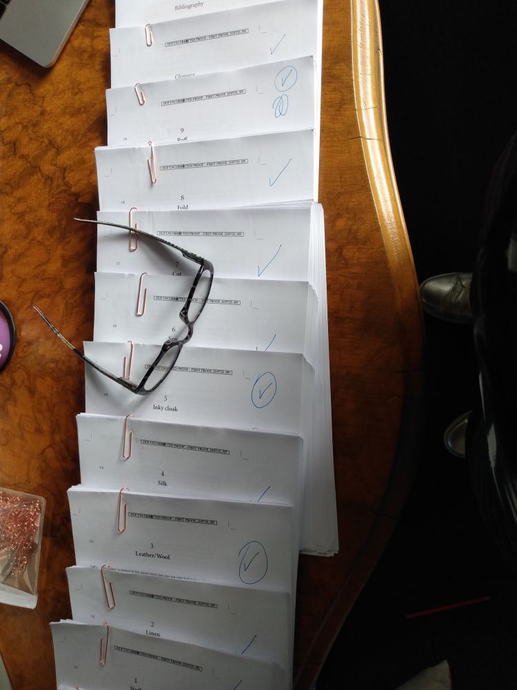 A photo from above of papers fanned out on a table, with individual piles paper-clipped together. A pair of reading glasses are resting on top. 