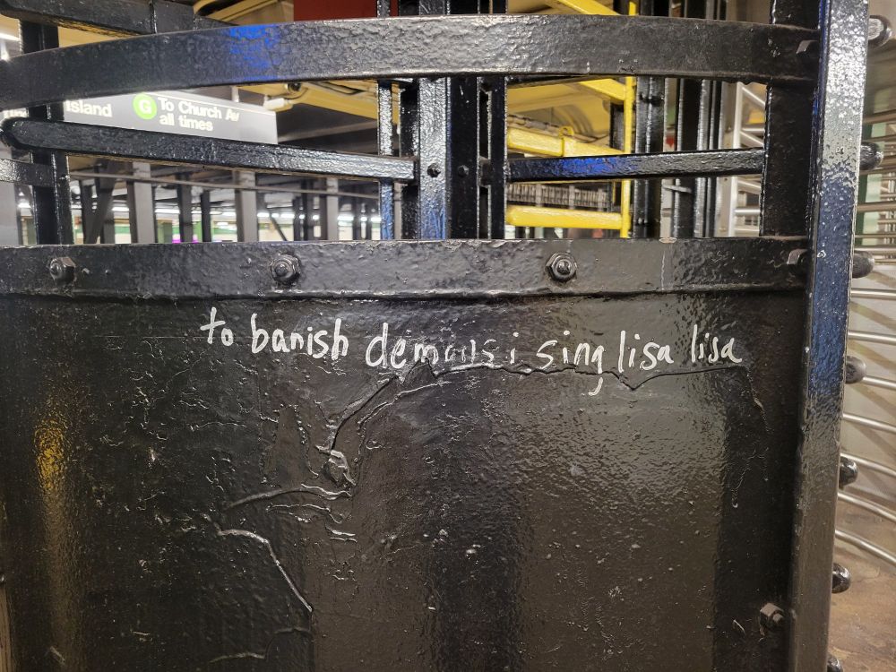 Photo of a subway turnstile on which someone has graffitied, "to banish demons, i sing lisa lisa."