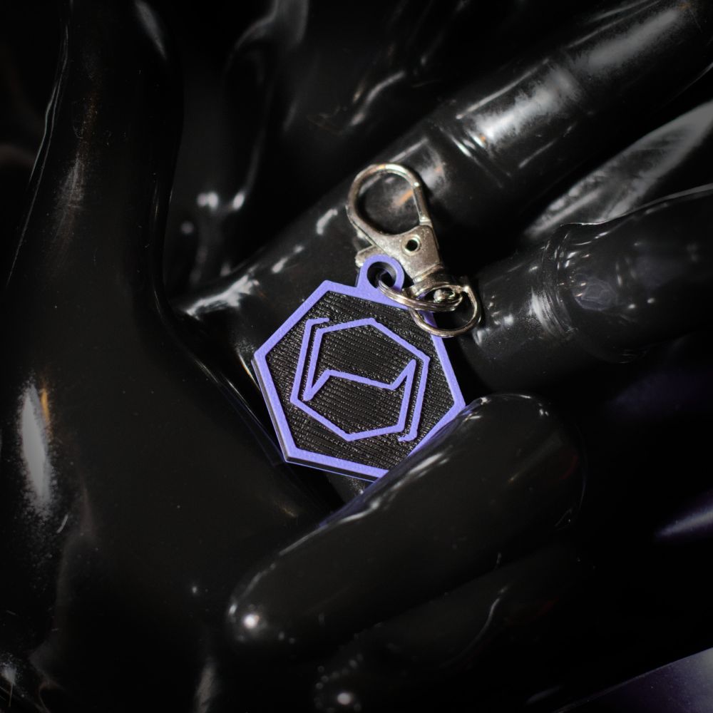 A printed hexcorp keychain in a gloved rubber hand.