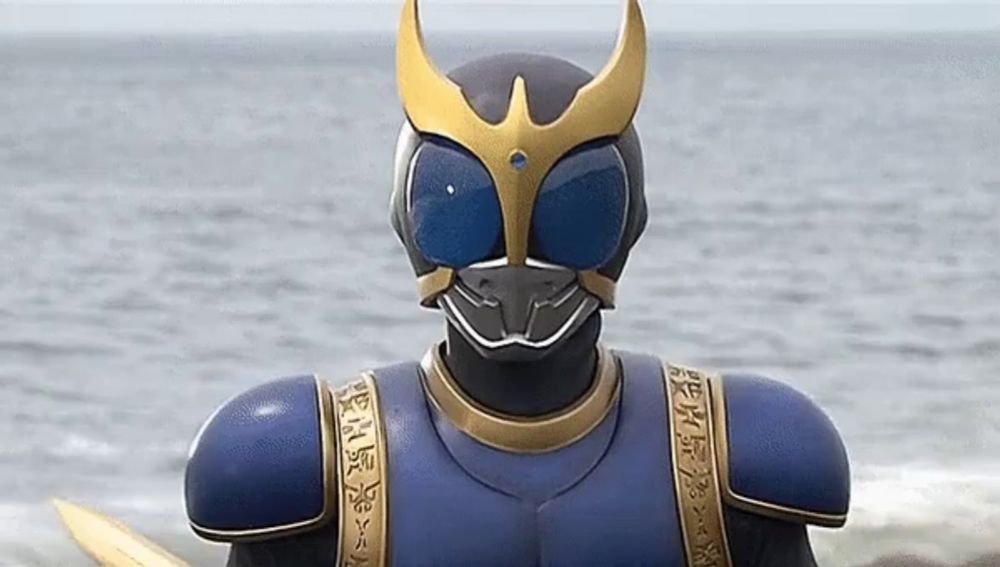 a statue of a superhero wearing a blue and gold costume stands in front of the ocean