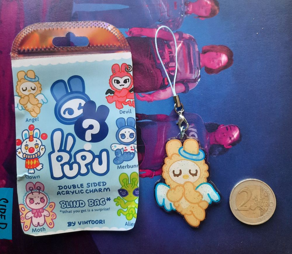 Photo of the angel charm with its packaging and 2 euro coin for scale.