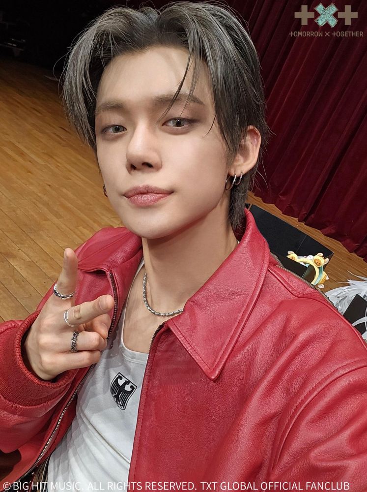 No-Labels-fan-sign-event-selfie YJ. Red pleather jacket. Little white graphic tee/tank top underneath. Tiny silver necklace. Rings on his fingers (while doing a peace sign). The greyish hair. Big hoop earrings!!!!!!!!!!