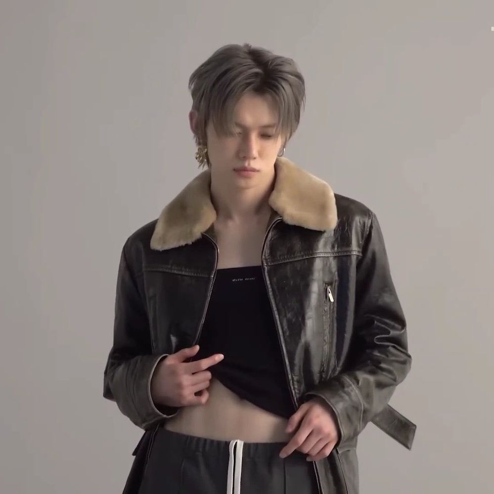 Magazine shoot for YJ. Pilot jacket with the fuzzy collar. Pants with drawstrings sticking out. Black shirt underneath being pulled up & revealing a belly button. Gray hair. Big earrings. 