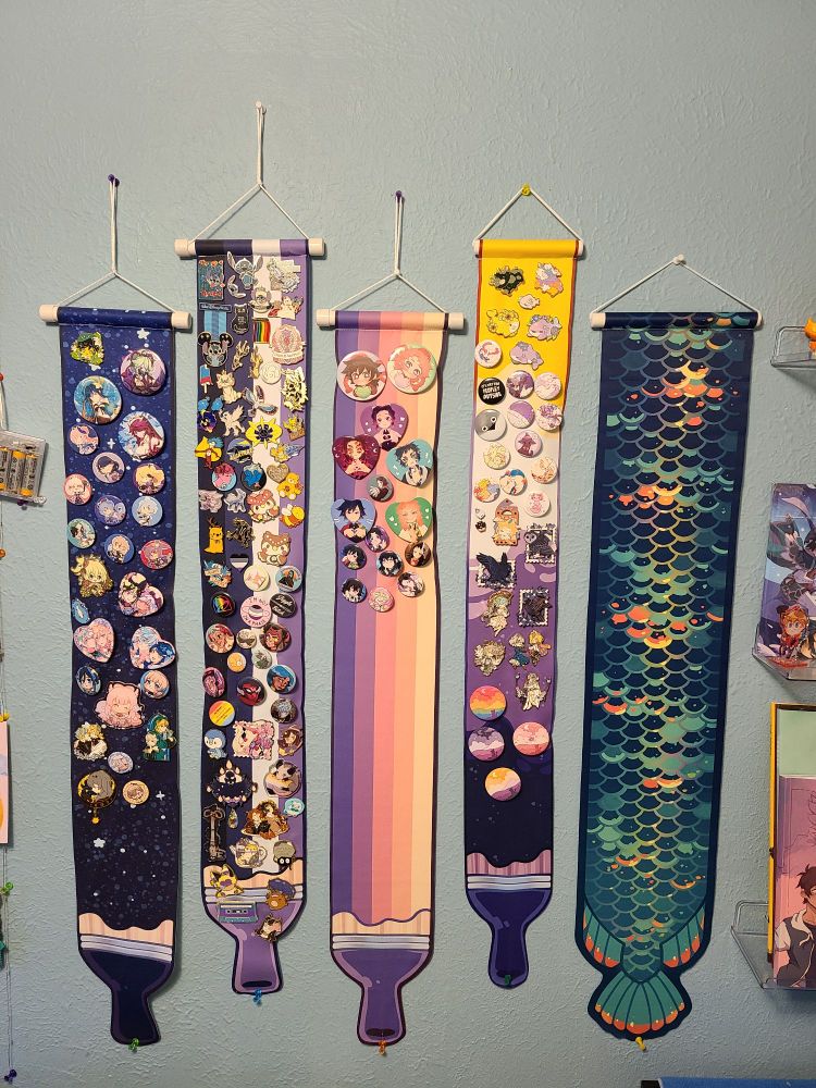 Photo showing off 5 pin banners, one being a paintbrush with the night sky, one being a paint brush with the asexual flag colors, one being a paintbrush with sunset colors, one being a paintbrush with the nonbinary flag colors, and lastly one being fish scales of pretty teals and accent colors 
