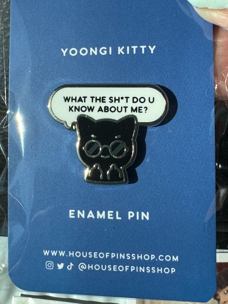 A Yoongi pin from House of Pins. It’s a black cat wearing sunglasses and extending both middle fingers. A speech bubble over his head says: WHAT THE SH*T DO U KNOW ABOUT ME?