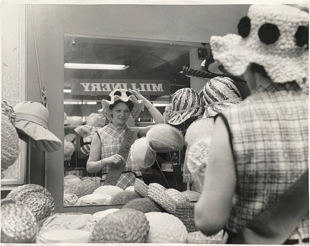 A woman trying on a hat and looking in a mirror surrounded by more hats