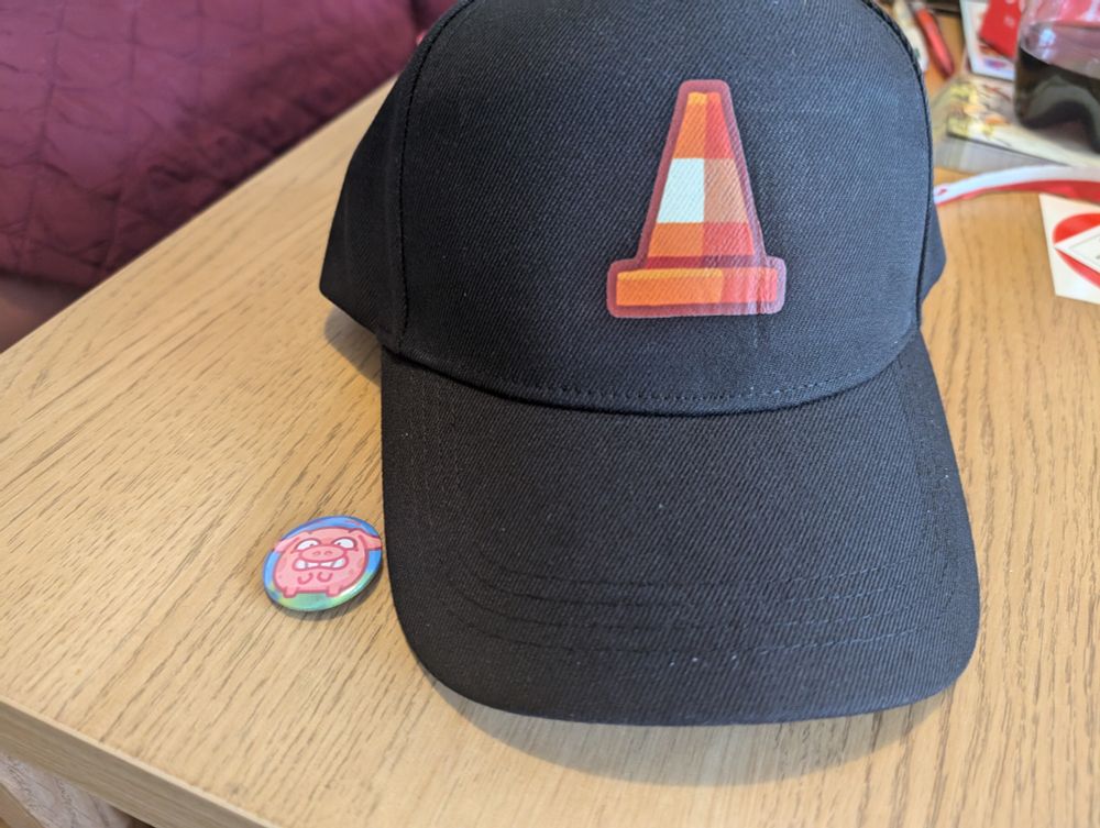 A styscraper pig pin badge and a cap with a styscraper traffic cone.