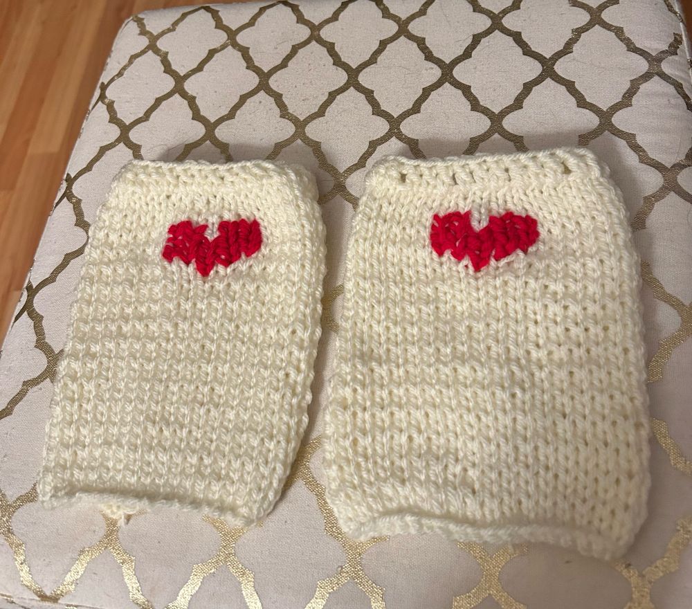 Two rectangular knitted boot cuffs, cream colored yarn, red heart knitted into the top center of each 