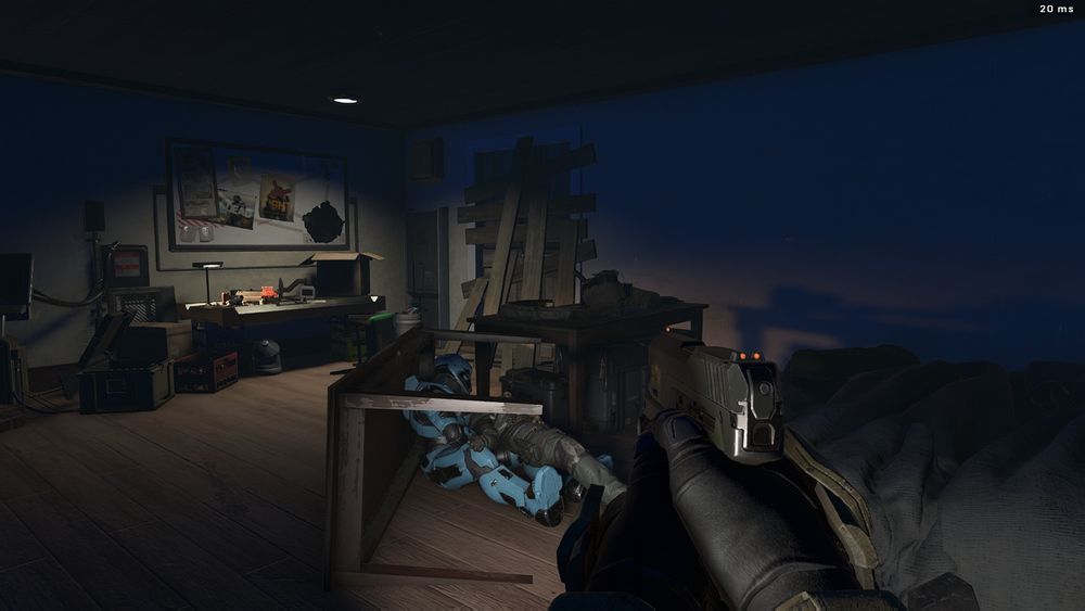 Screenshot from Halo Infinite Forge. A first-person perspective of a dimly lit room, the entrance door barricaded with planks, and a messy desk in the background. An overturned table has two slumped, armoured figures pushed against it.