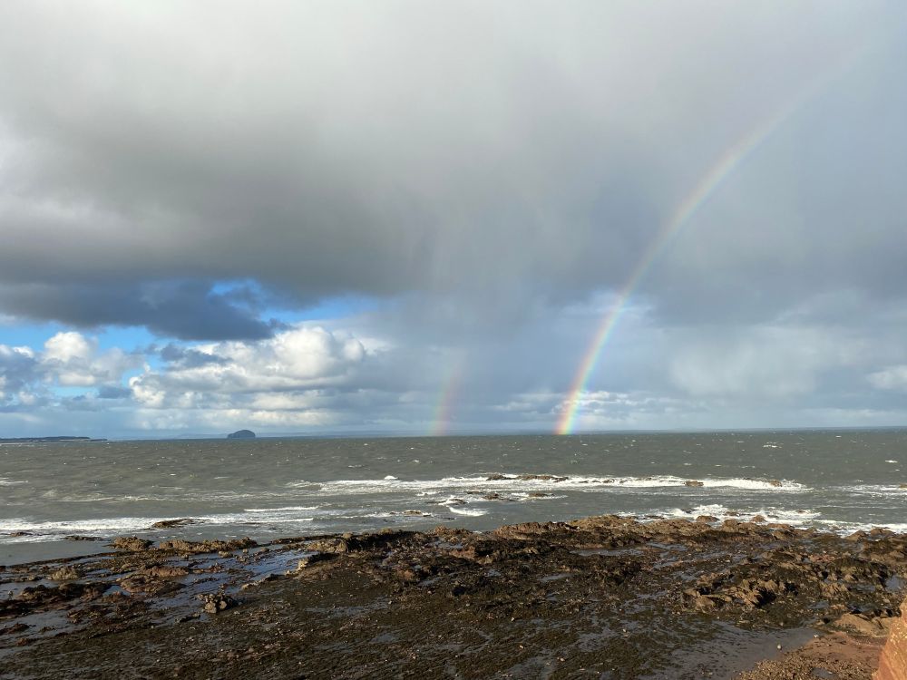 Photograph of a double rainbow over a choppy coast.