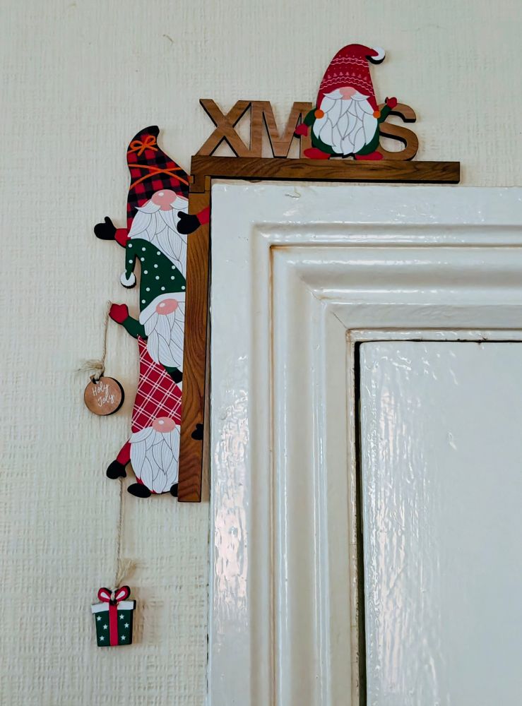 A wooden Christmas decoration over the corner of a doorway, with several Santa figures holding decorations, one a bauble inscribed with the words 'Holy Joly'