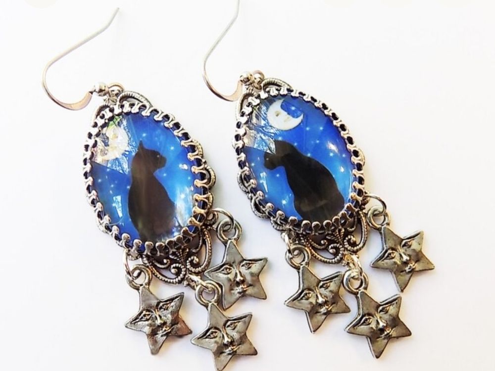 Over cabochon earrings in a silver tone setting with matching black cats in front of a starry night sky, with moon. Three star charms dangle from the bottom.
This and other delights available at https://www.etsy.com/shop/NomadicMoonArts