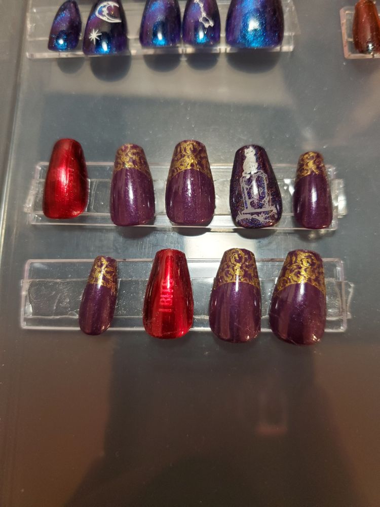 The closest I could get to a French manicure referencing Astarion's base armor from Baldur's Gate 3. They're a deep purple cream base with swirling filigree holographic gold tips stamped on. There are two shiny metallic red nails that should say, 