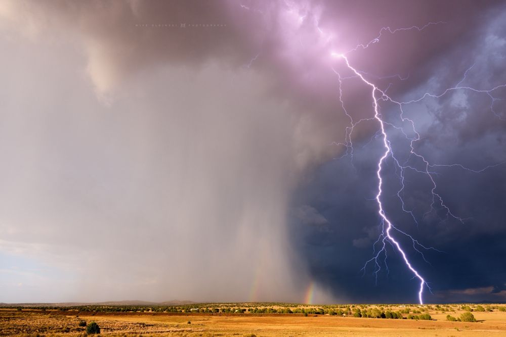 Lightning bolt with a small sliver of a double rainbow on the rain foot