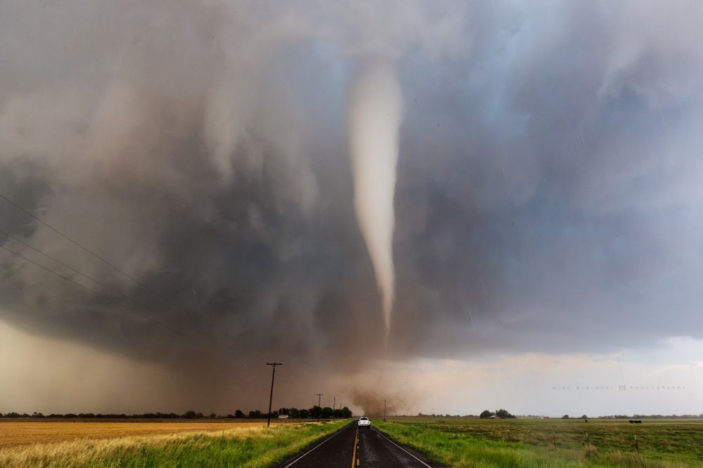 A white tornado down the middle of a road with a truck headed towards it 