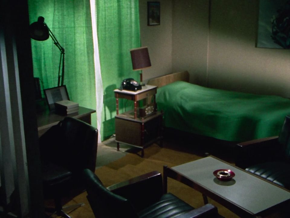 KR '71 ep 11, Hongo's bedroom. The drawn blinds are the same green as the bedspread, the bed frame is a wooden western style one, and there's a white & brown coffee table in one corner