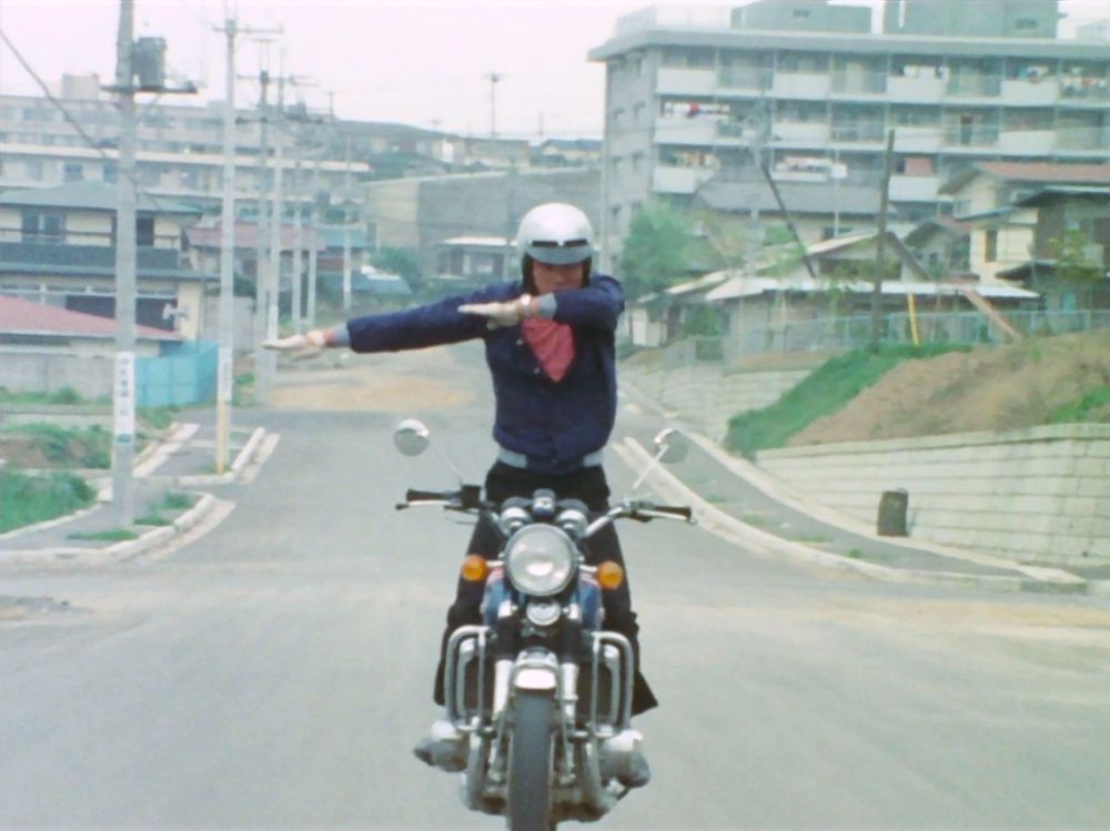 Straight on view of Kazami doing his henshin pose while standing on his bike in motion
