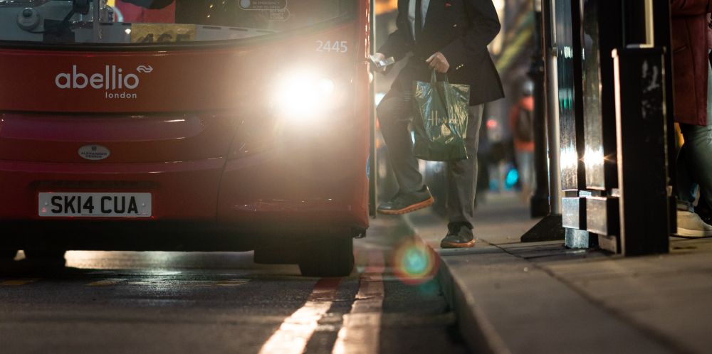 A man steps from the pavement onto a bus at night time