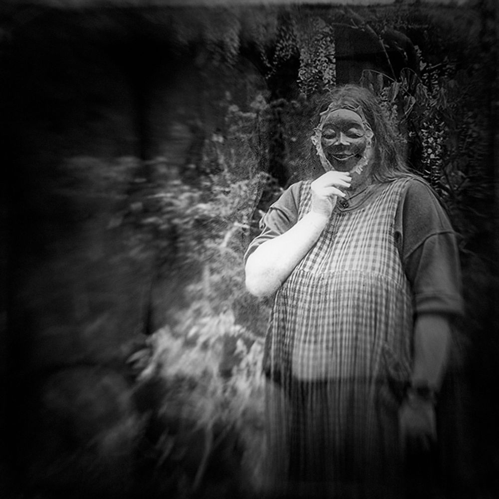 A large woman, who did not want to be photographed, poses while holding up a mask to her face.