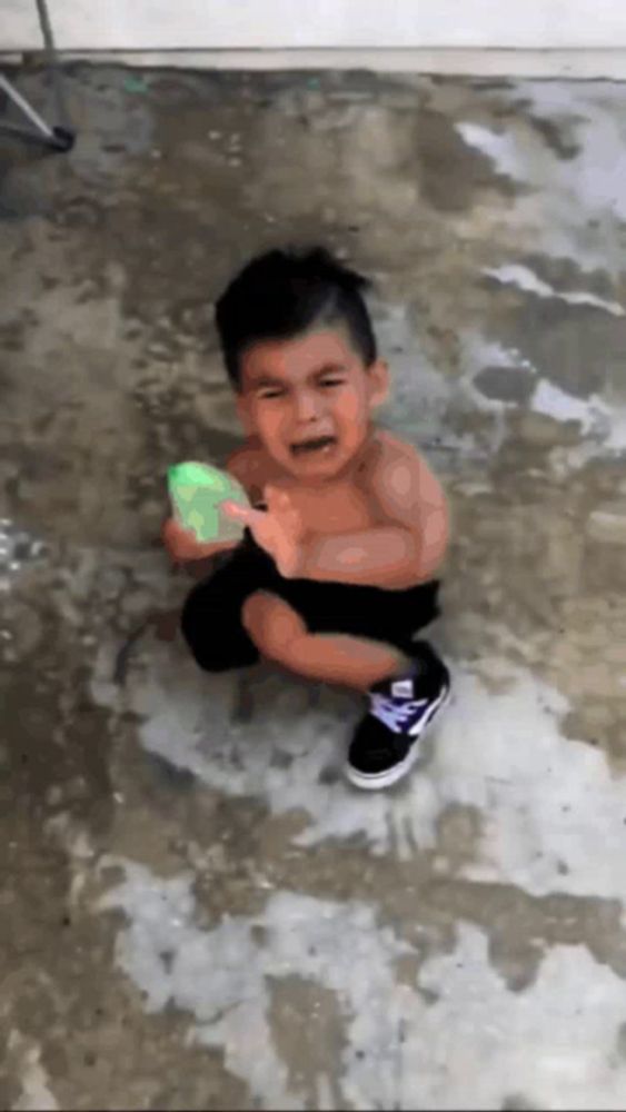 a little boy is crying while holding a green water gun