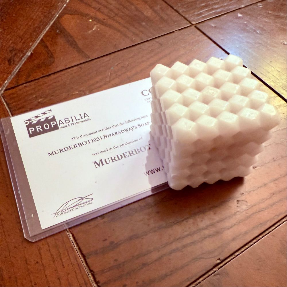 Photo of a bar of prop soap that is a square made of many hexagons. A certificate of authenticity is below it on the table