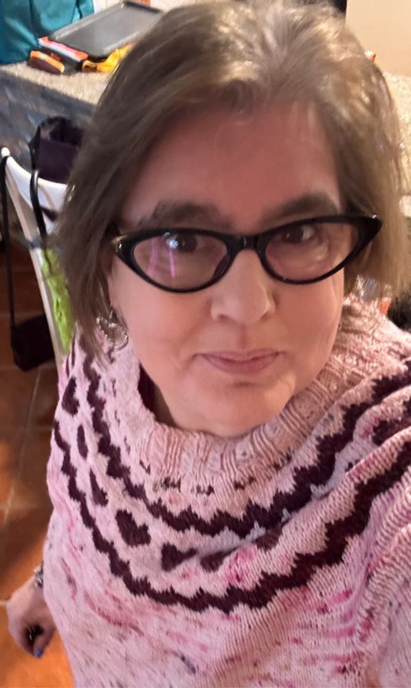 White woman wearing a pink handknit sweater with burgundy hearts. 