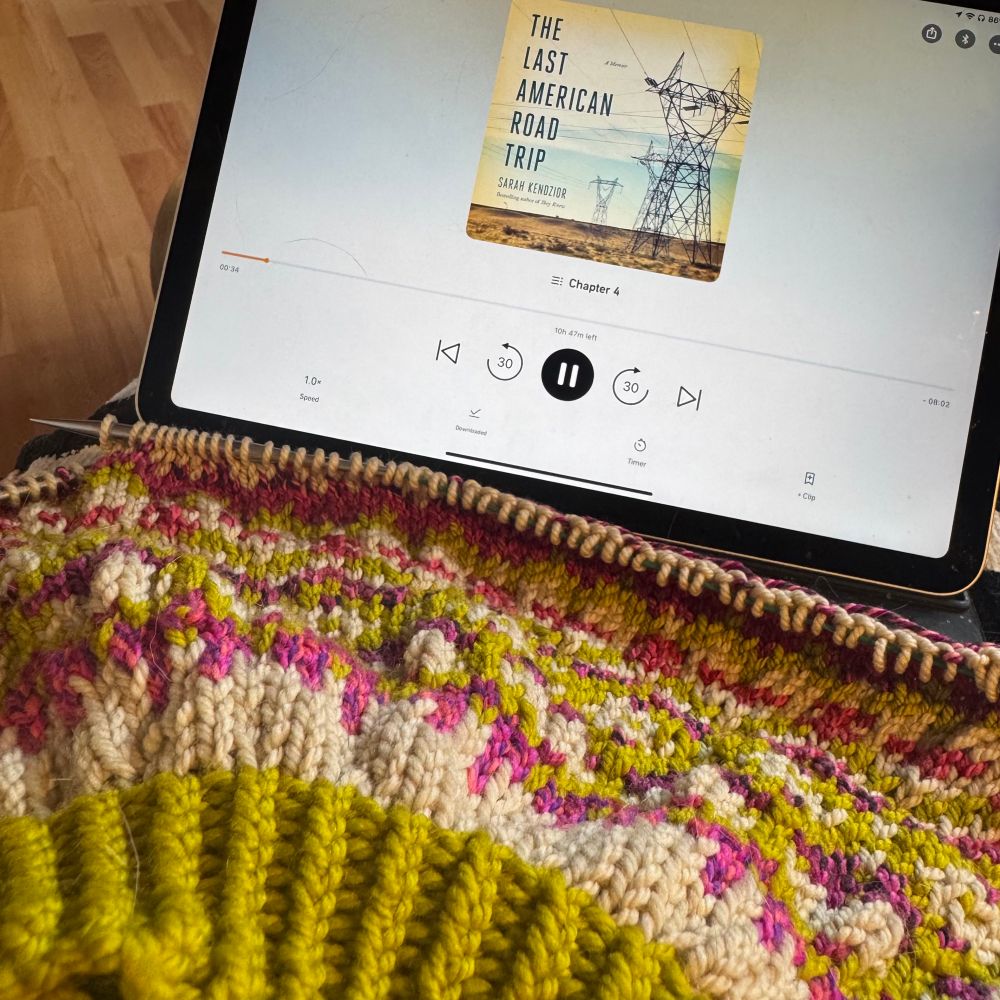 Pink, green, and white colorwork yoke with iPad playing The Last American Road Trip
