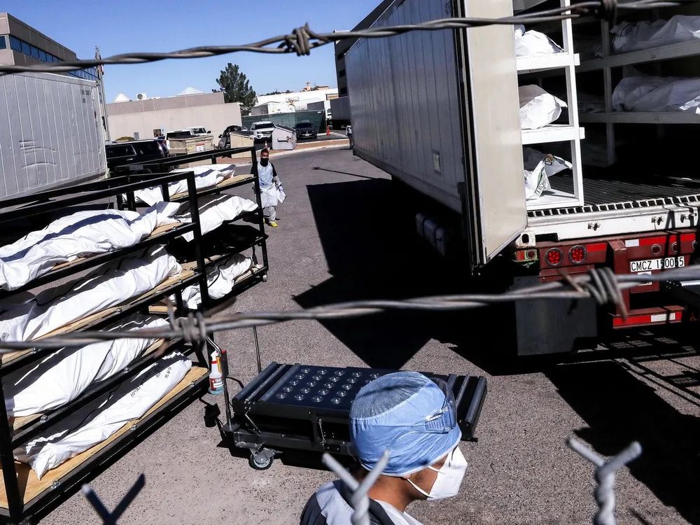 A refrigerator truck being loaded with multiple, stacked carts of body bags