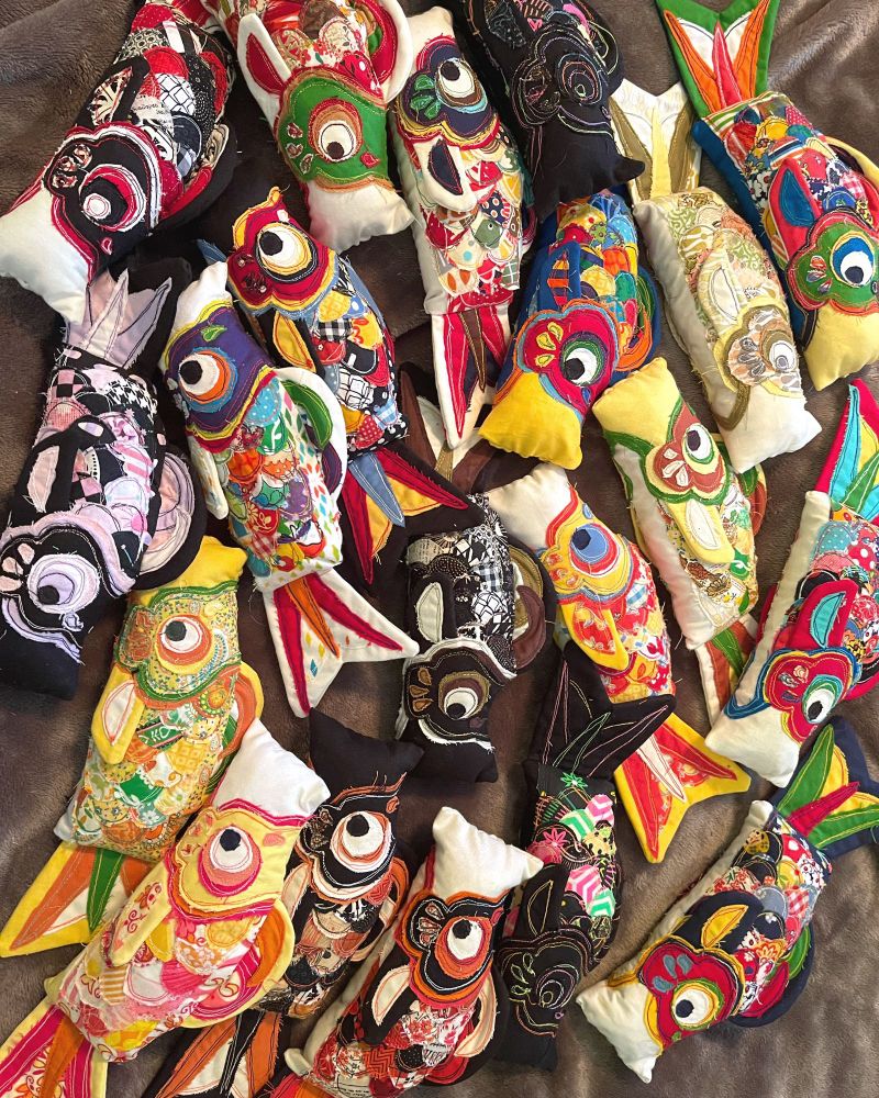 About 20 small stuffed carp plushies that resemble Japanese koi flags on a grey background