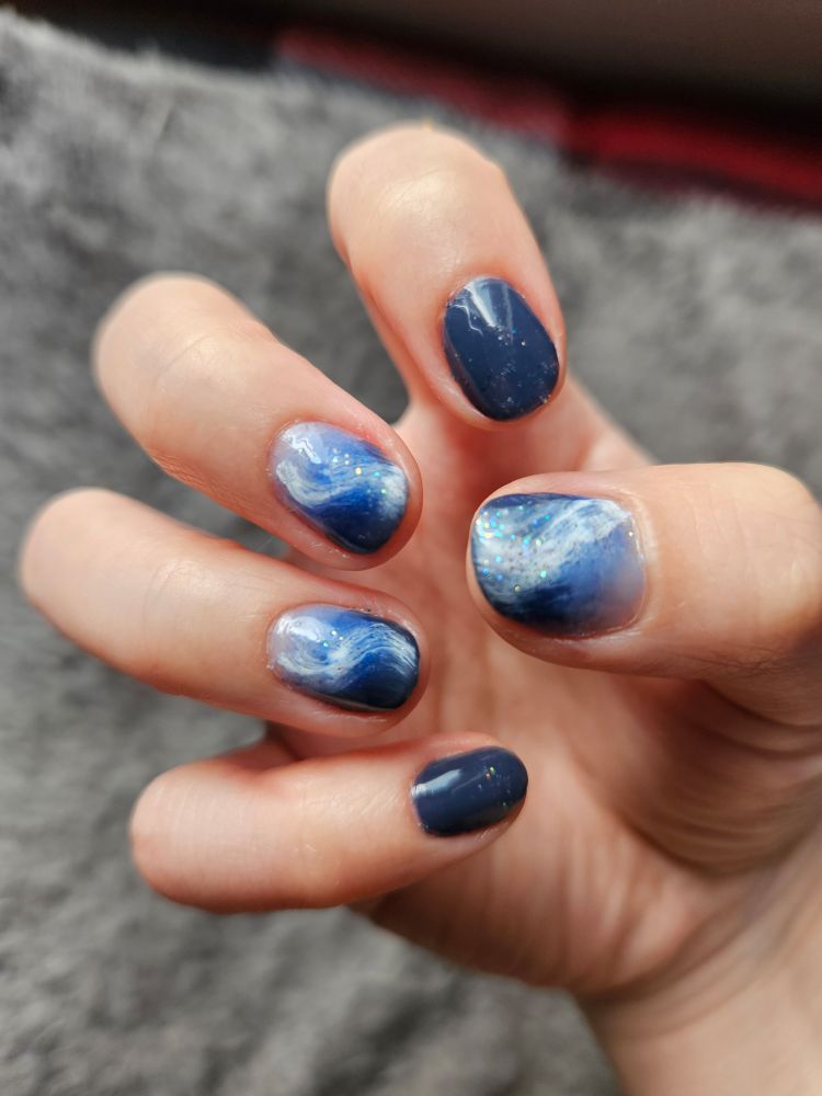 A photo of short nails painted with blue to white gradient polish. A white swirl and sparkles top the middle, ring and thumb.