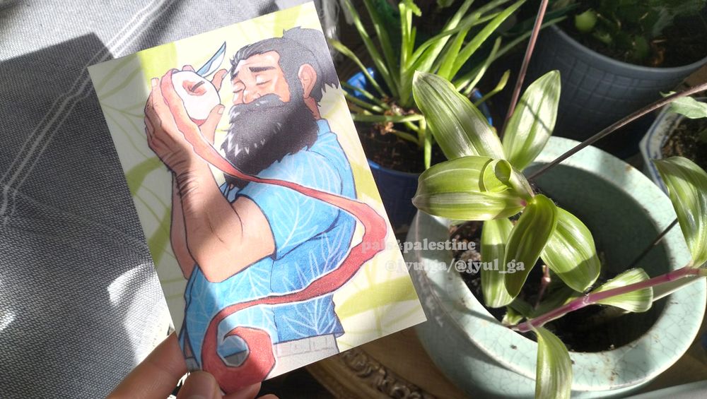 Photo of a postcard held up under sunlight shining in from a window, next to a group of potted plants. The postcard has a subtle glitter finish, and features an illustration of Senshi from Dungeon Meshi peacefully peeling an apple. 
