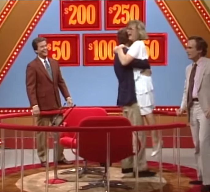A player picks up Laurie Hendler completely off the ground after winning $10,000. Dick Cavett and Dick Clark look on 
