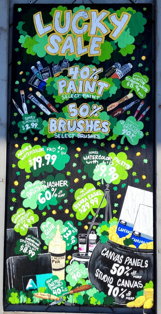 A hand-painted sign, advertising art products, in the theme of shamrocks and coins. 