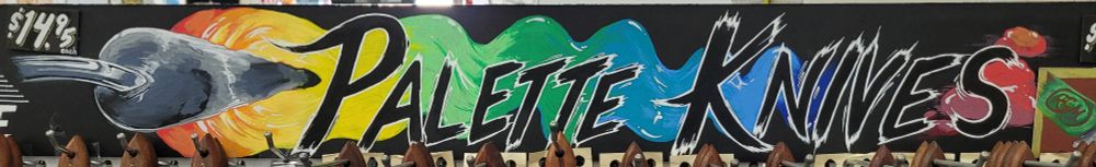 A large hand-painted sign stating Palette Knives overlaid on a rainbow paint with the end of the palette knife on the far left. 