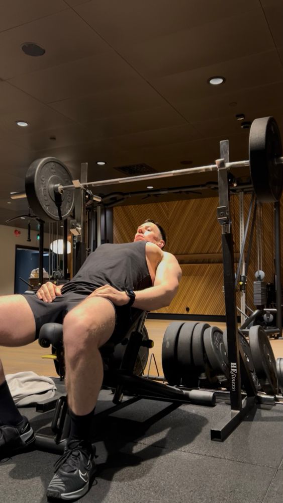 Me on an incline bench in the gym under a barbell. You can see my pecs really prominently out of the side of my vest. 